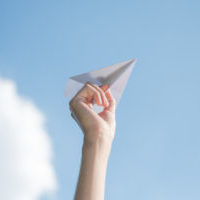 Men's hands holding a white paper rocket with a bright blue background.